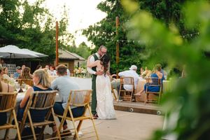 Outdoor evening wedding reception with guests dining at round tables decorated with white linens under string lights.