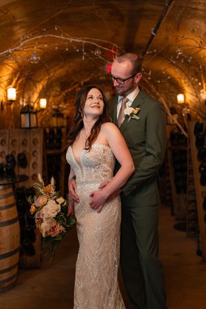 A couple shares an intimate dance moment in a rustic wine cellar with wooden barrels in the background.