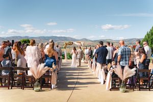 Outdoor wedding ceremony setup with guests seated in rows of wooden chairs on a paved area overlooking mountain views.