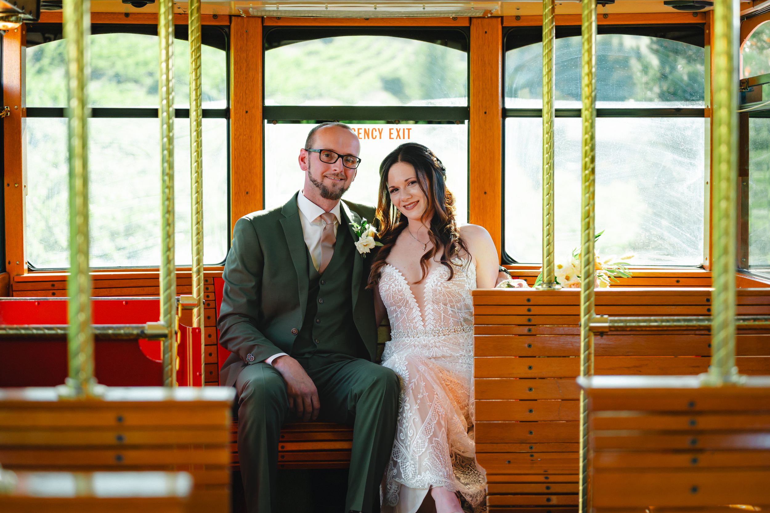 Newlyweds seated together inside vintage wooden trolley car with natural light streaming through windows.