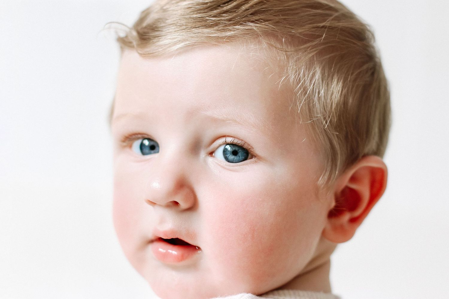 Baby with bright blonde hair and striking blue eyes  during birthday shoot at cost home photography studio in Nottingham