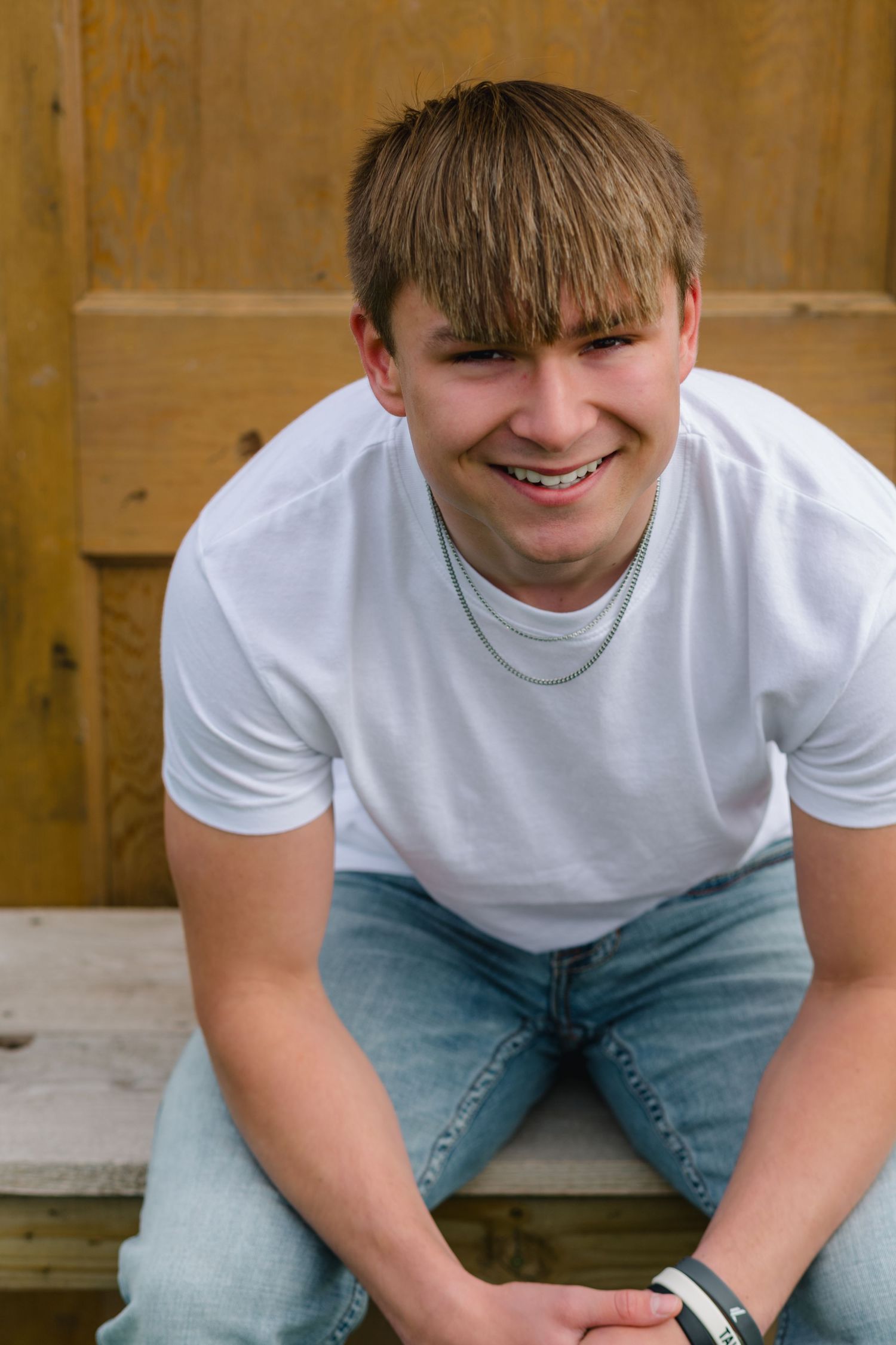 A joyful smile and casual pose in a white t-shirt and light blue jeans against a wooden backdrop.