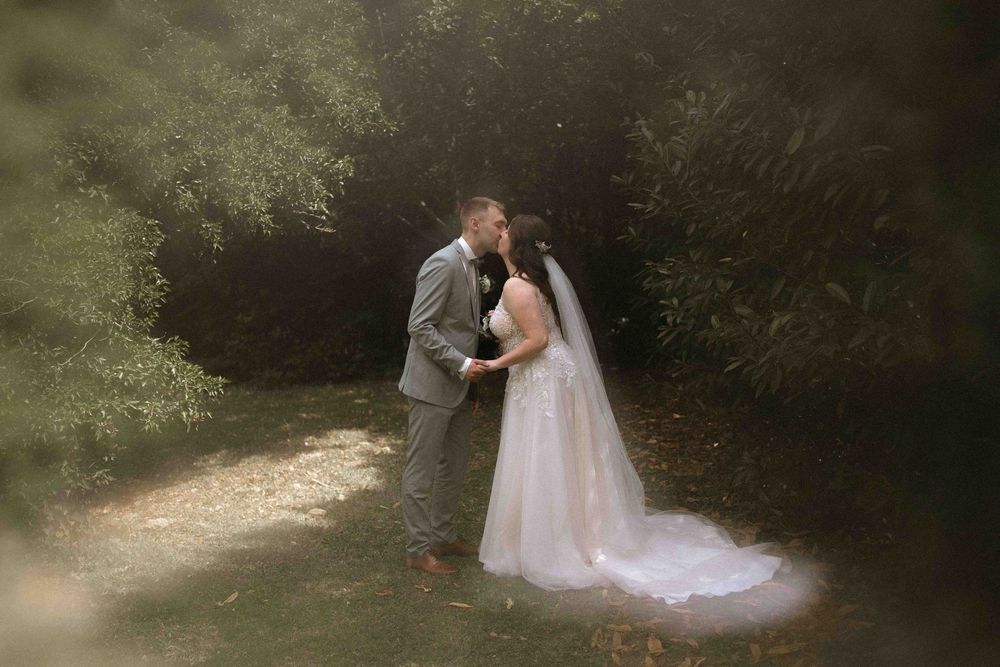 Couple shares intimate wedding moments in a sunlit wooded area.