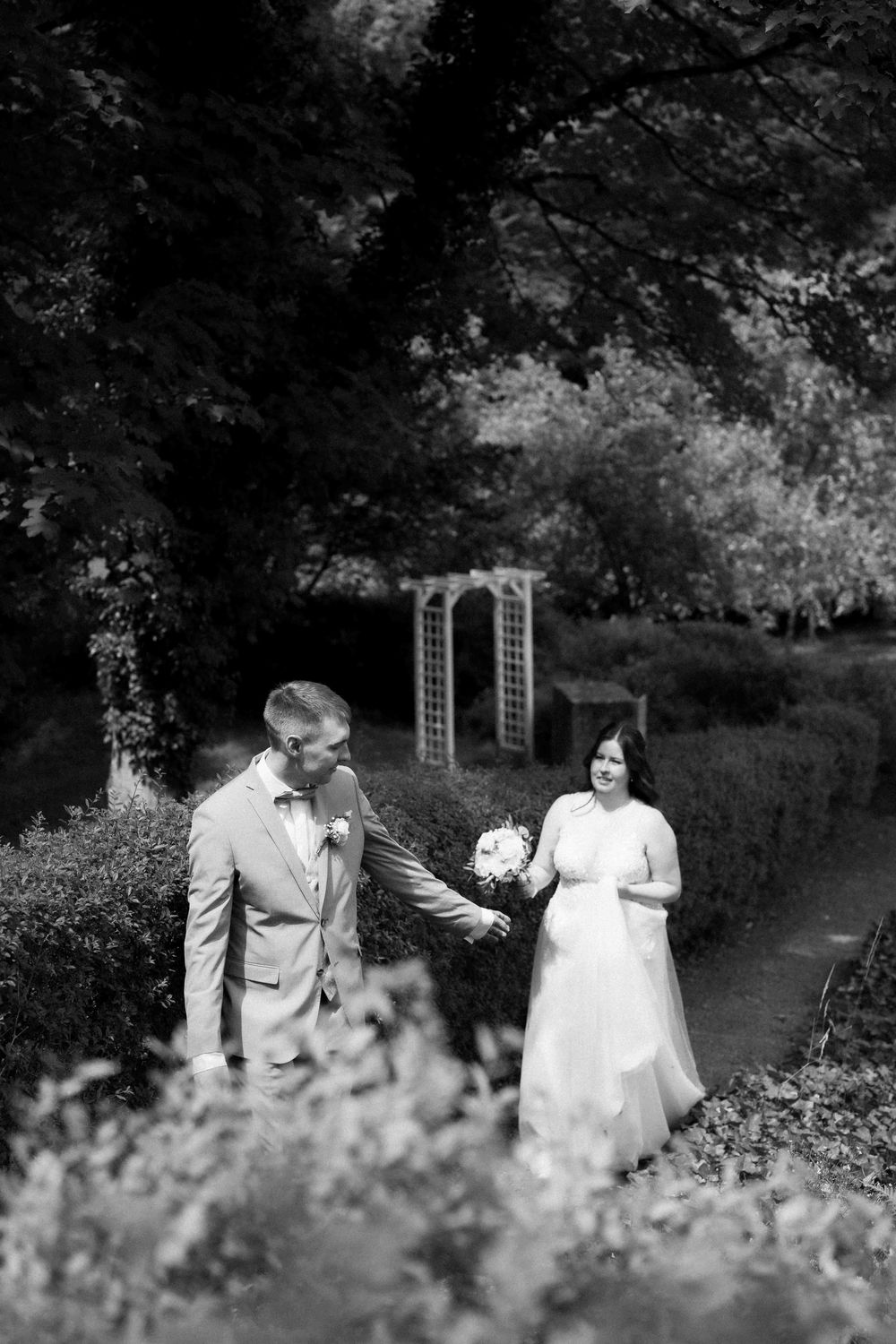 Black and white garden wedding photo with couple standing among blooming flowers near an arbor.
