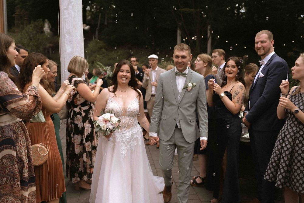 Wedding guests throw confetti and celebrate as the newlyweds walk through a crowd.