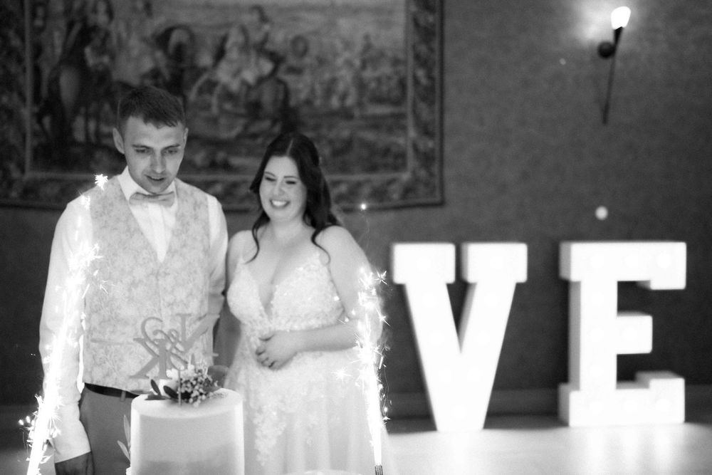A black and white photo of a couple beside their wedding cake with illuminated LOVE letters.