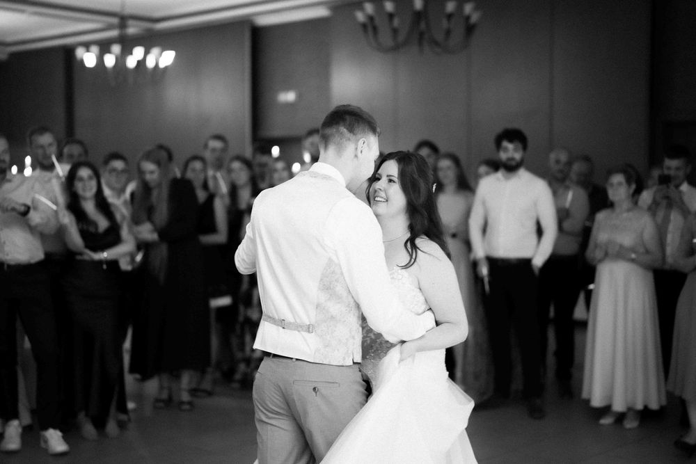 A couple shares a romantic first dance at their wedding reception while guests look on in black and white.