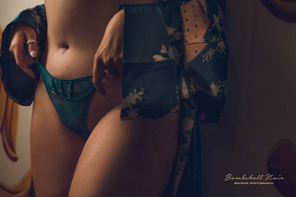 A dark and moody boudoir photoshoot featuring a woman in blue lingerie posing on a bed against a shadowy backdrop.