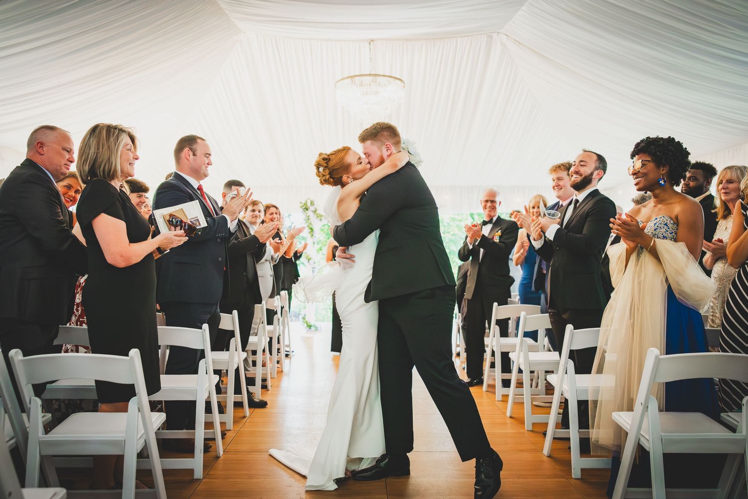 Elegant wedding guests seated in white chairs inside a bright modern venue with draped white fabric ceiling at the Overhills Mansion