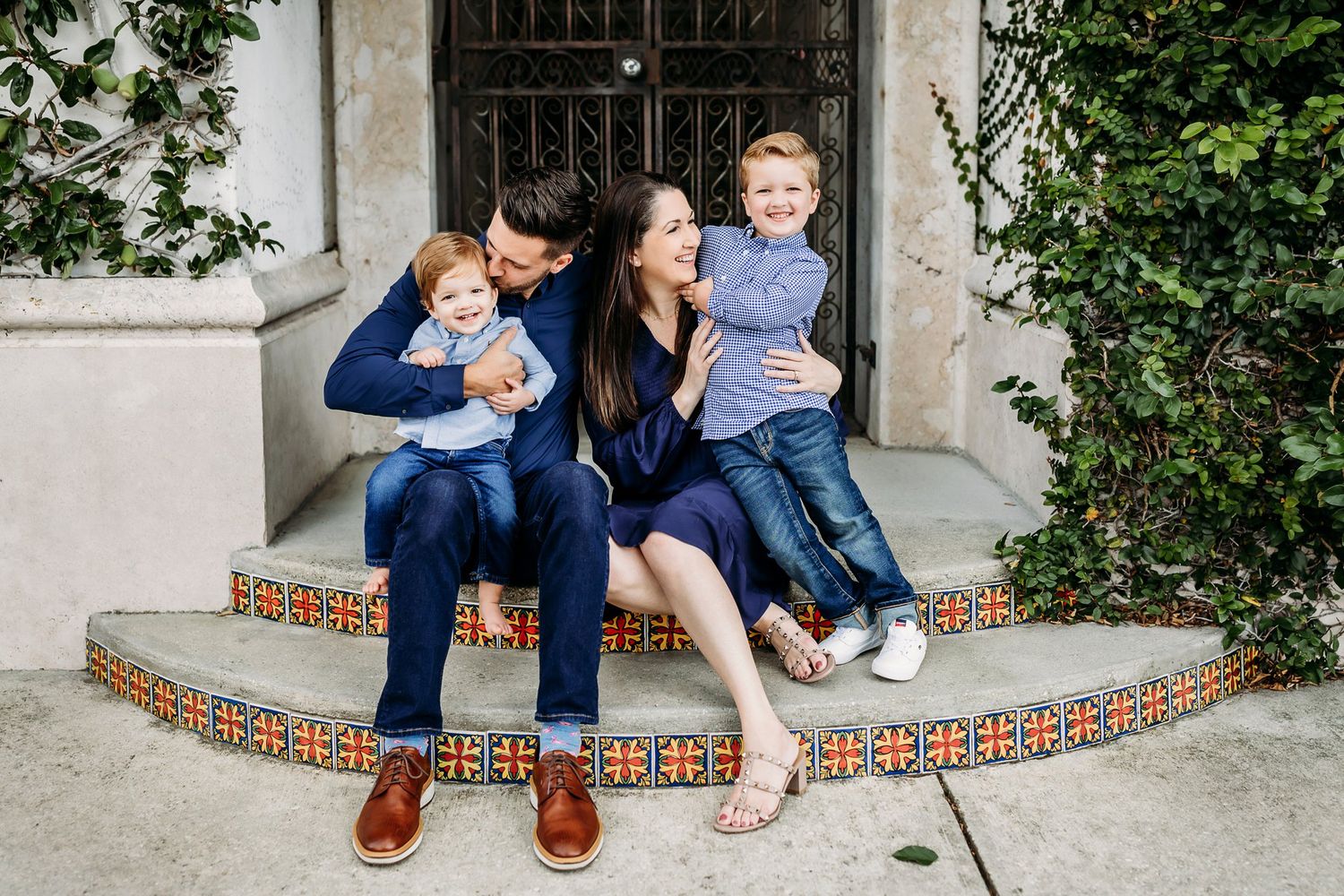 Smiling group sitting together on decorative tiled steps in front of an ornate doorway surrounded by greenery.