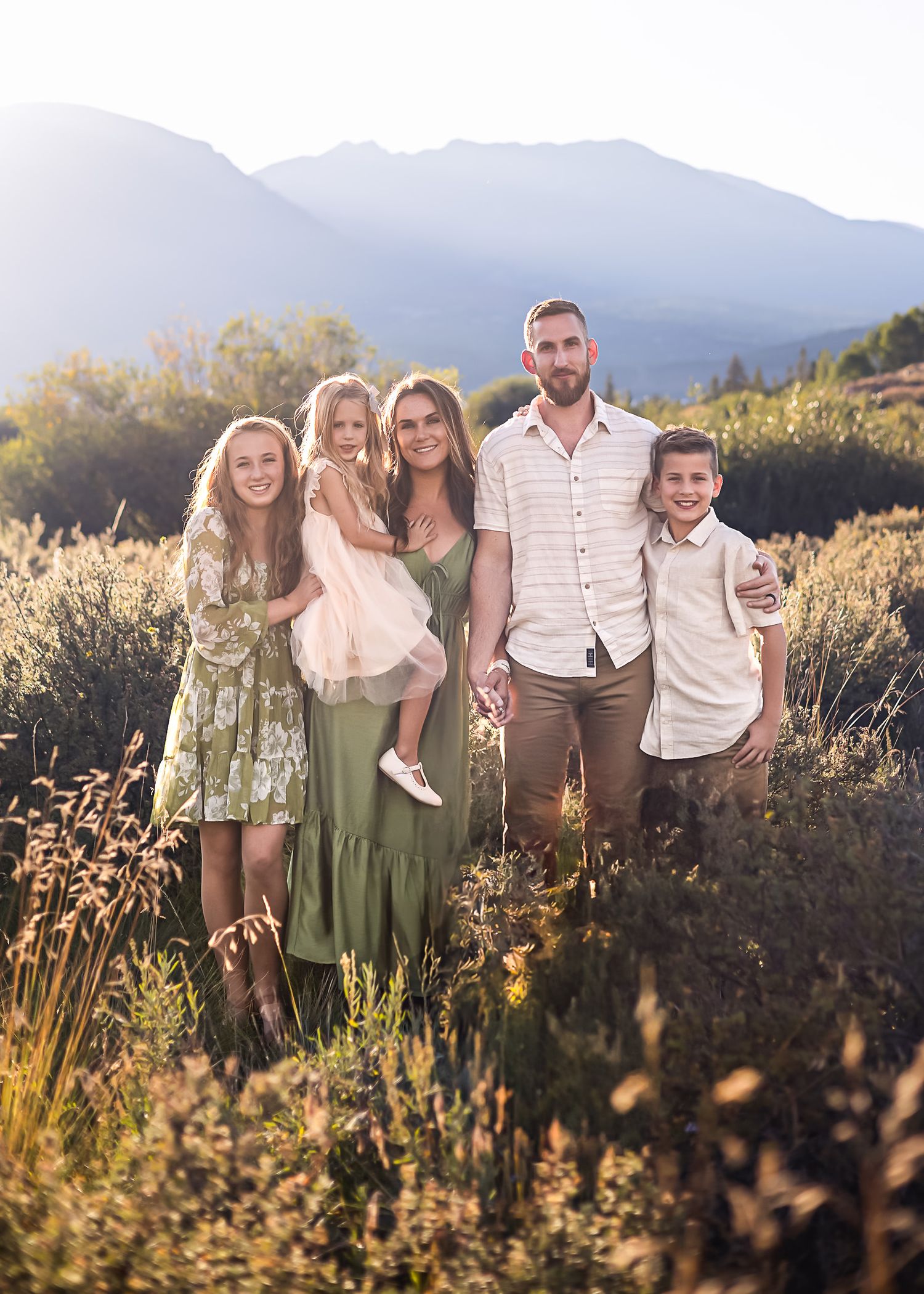 Family of five posing together in mountain field during golden hour.