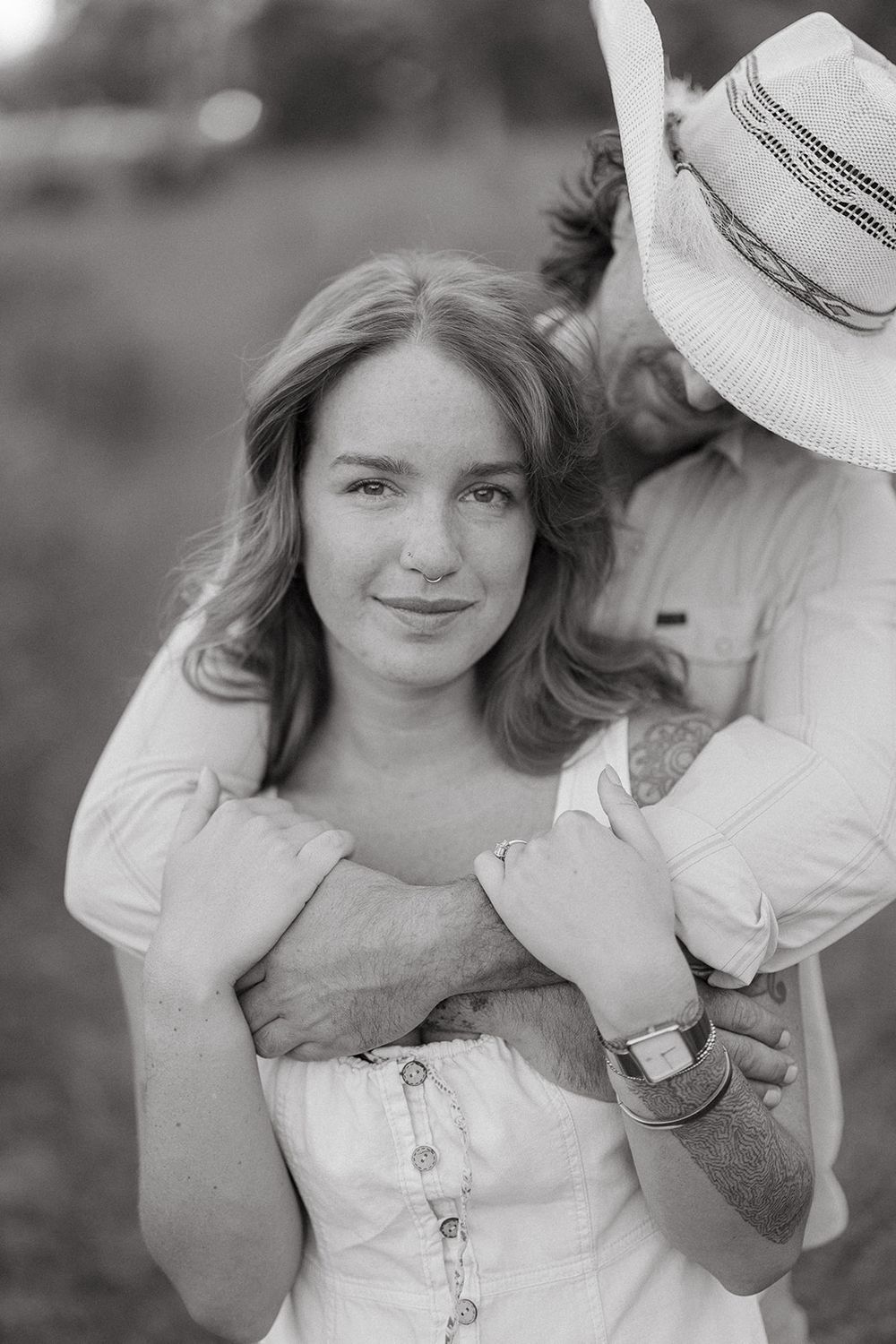 Black and white portrait of a couple embracing outdoors, with one wearing a white summer hat and the other in a corset top.
