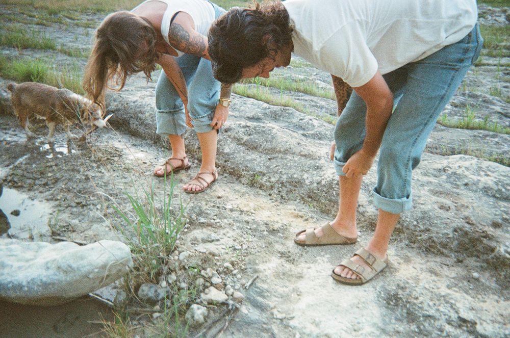 People examine rocks and fossils at a geologic site while wearing casual summer clothing and sandals.