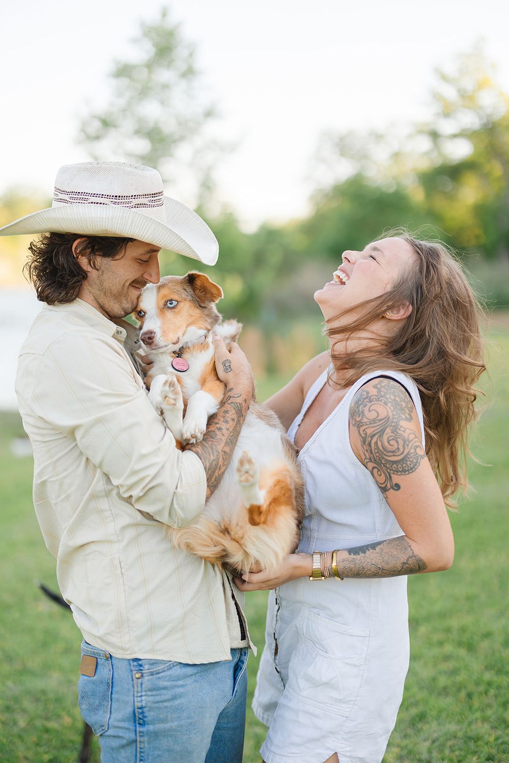 A couple plays with their cheerful brown and white dog in a sunlit outdoor setting.