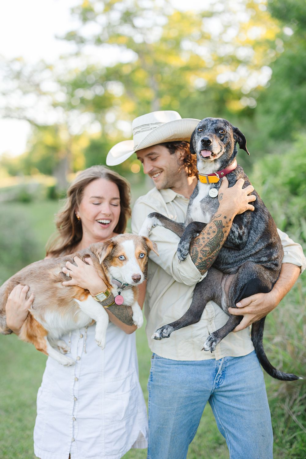 A couple shares joyful laughter while holding their two beloved rescue dogs outdoors on a sunny day.