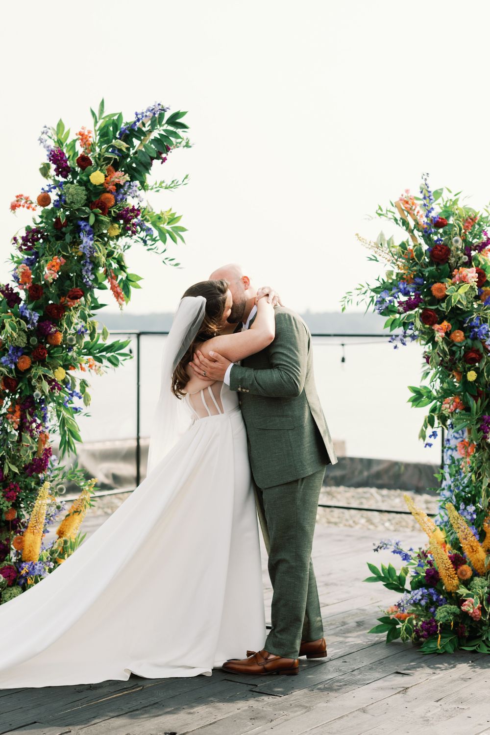 A romantic wedding couple shares a kiss against a beautiful floral arch in a sequence of photos.