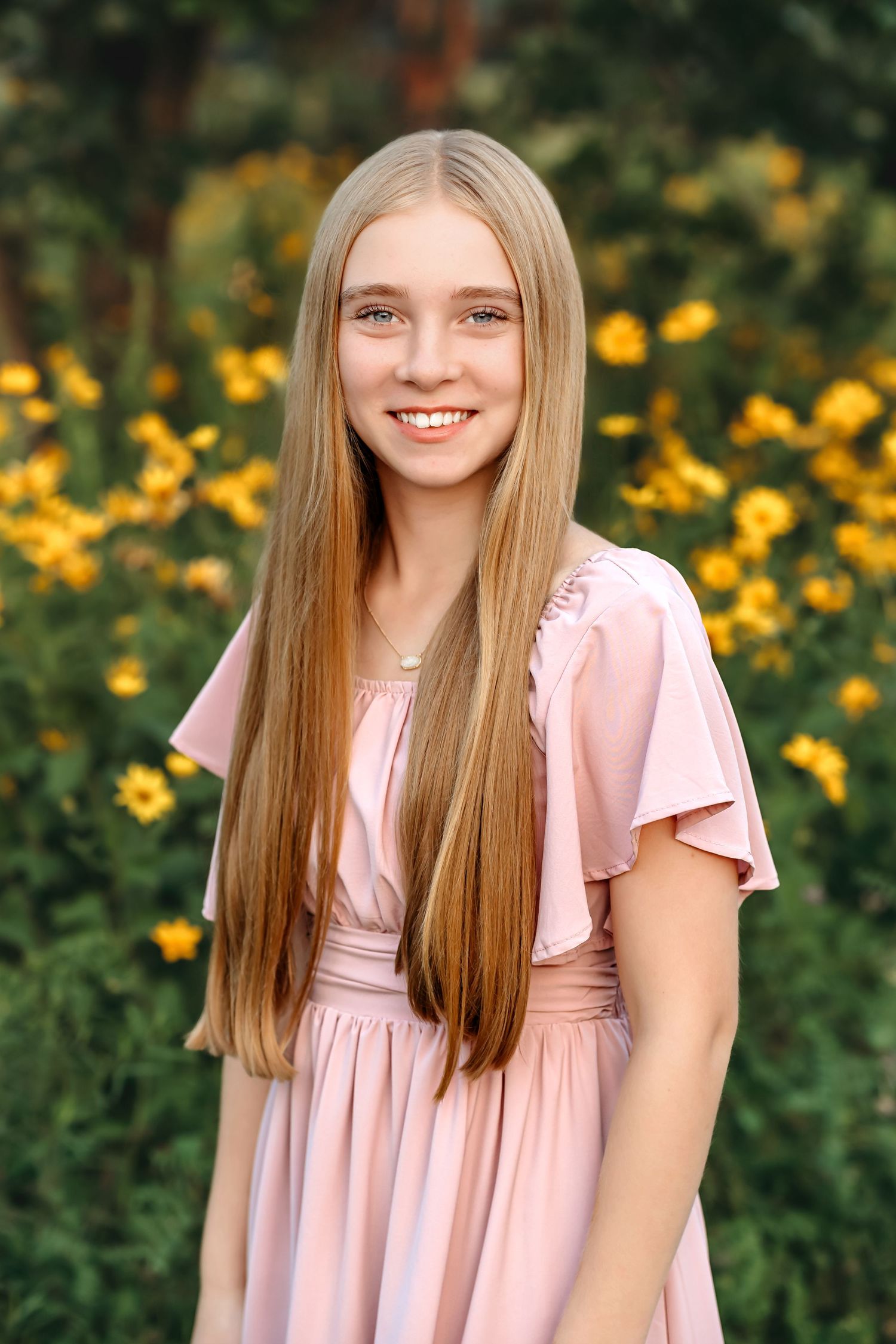 Young girl in a pink dress poses for portraits in front of blooming yellow flowers.