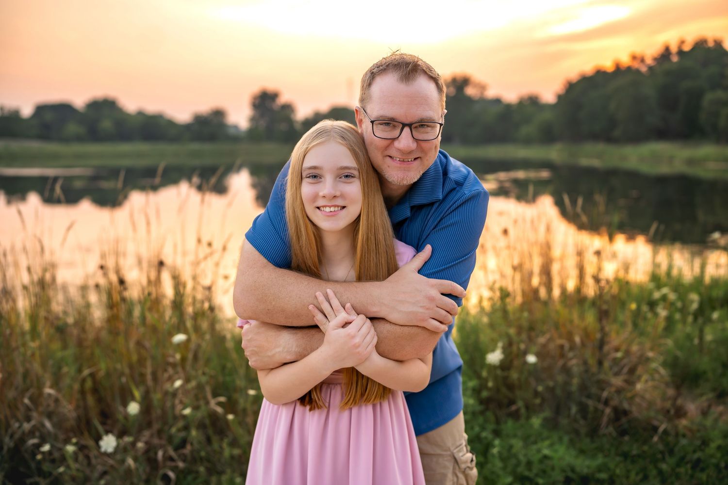 Two people embracing and smiling together by a lake at sunset with golden light reflecting on the water.