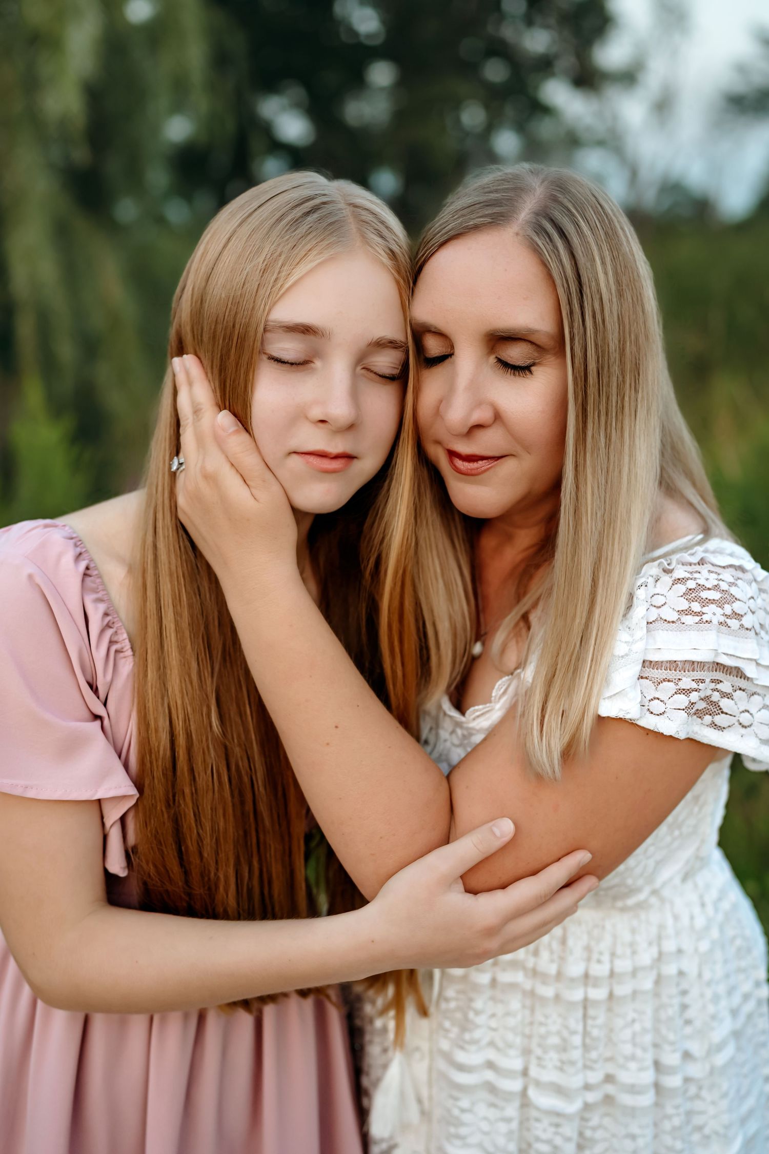 Two people in pink and white dresses share an intimate tender moment outdoors with soft lighting.