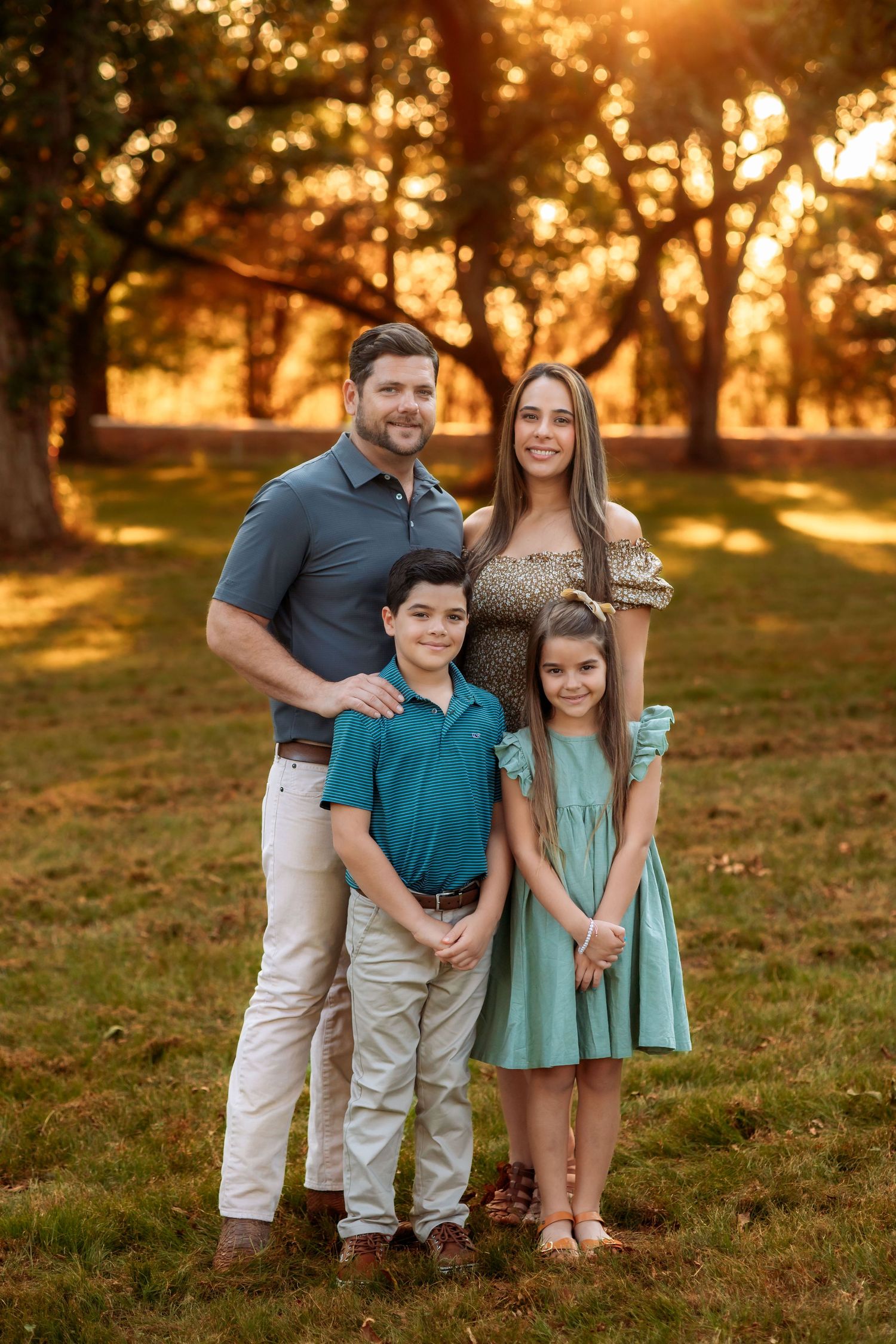 A family poses together outdoors in front of large rocks and trees during a sunny afternoon photoshoot.