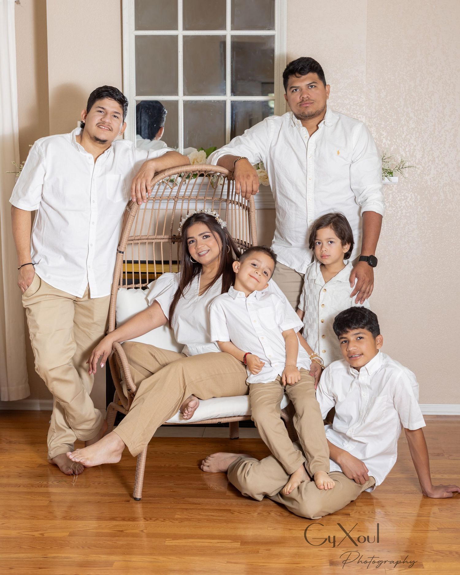 A family of six poses together in coordinating white shirts and khaki pants for a professional indoor portrait.