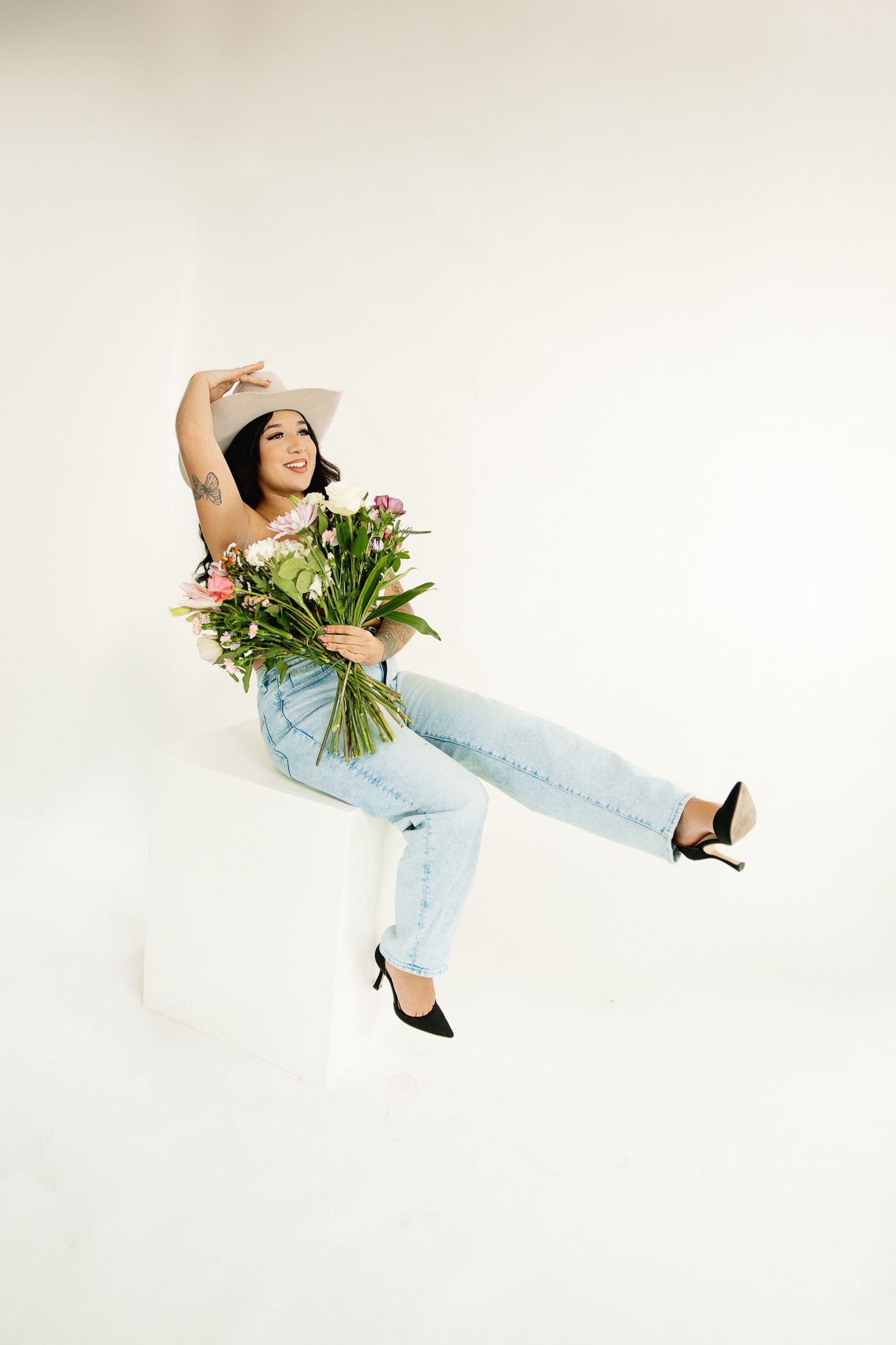 Studio birthday photoshoot of a cowgirl posing on a posing block while she celebrates with flowers in a colorado studio.