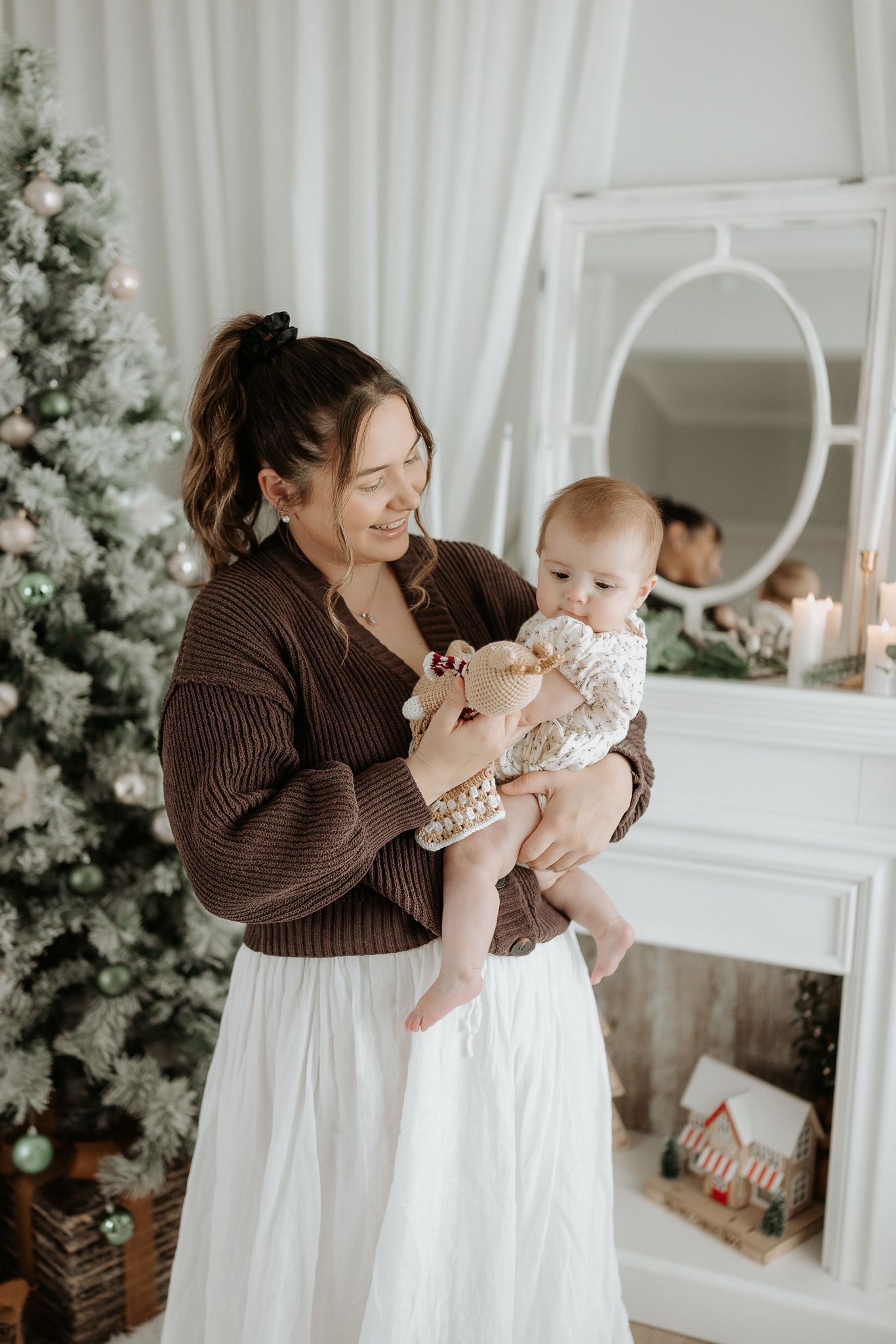 Little ones in white outfits share sweet moments and laughter in front of a snowy white Christmas tree in matching holiday photos.