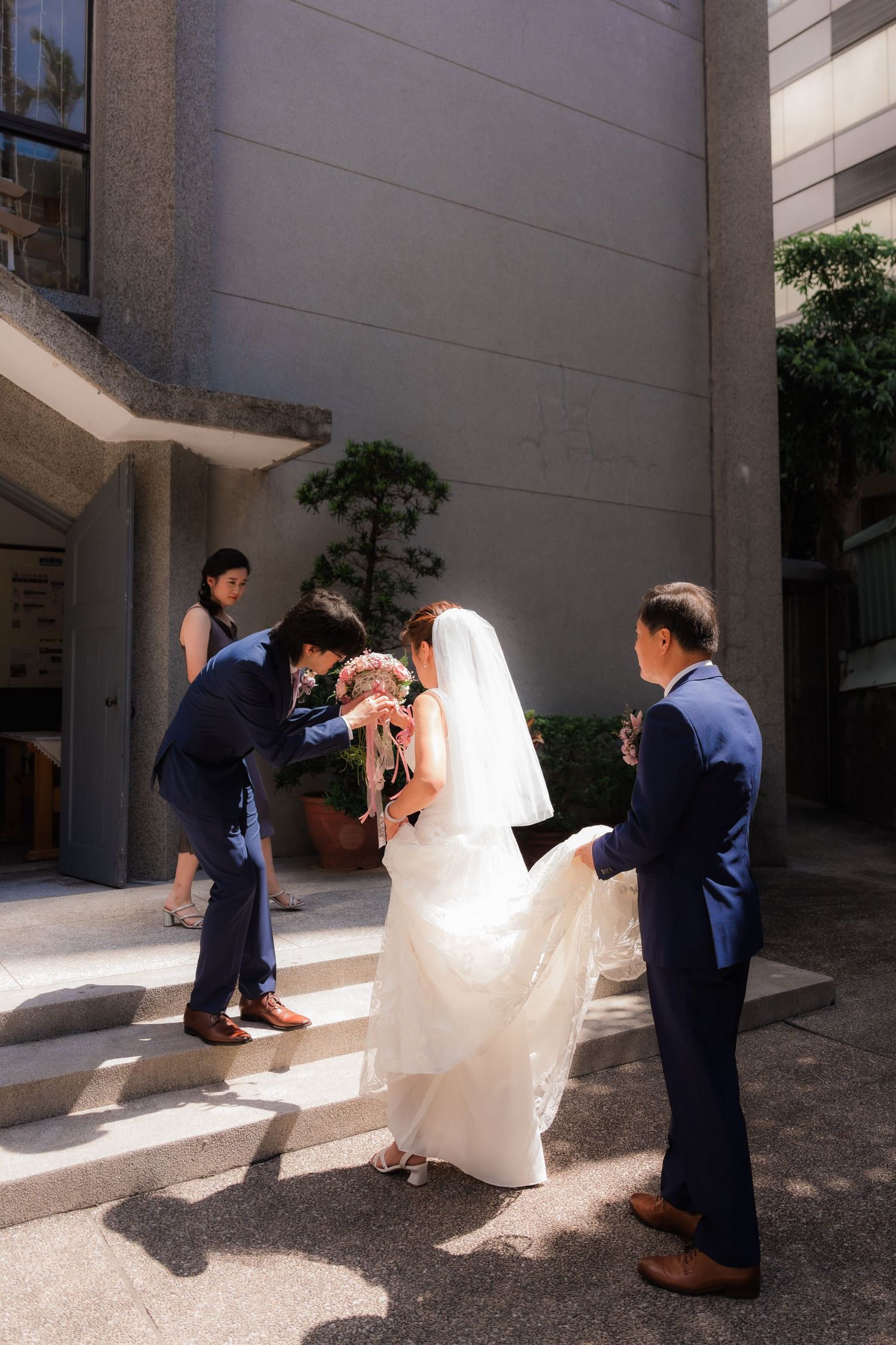 A sequence of wedding photos showing the groom getting down on one knee to help adjust the bride's dress in sunlight.