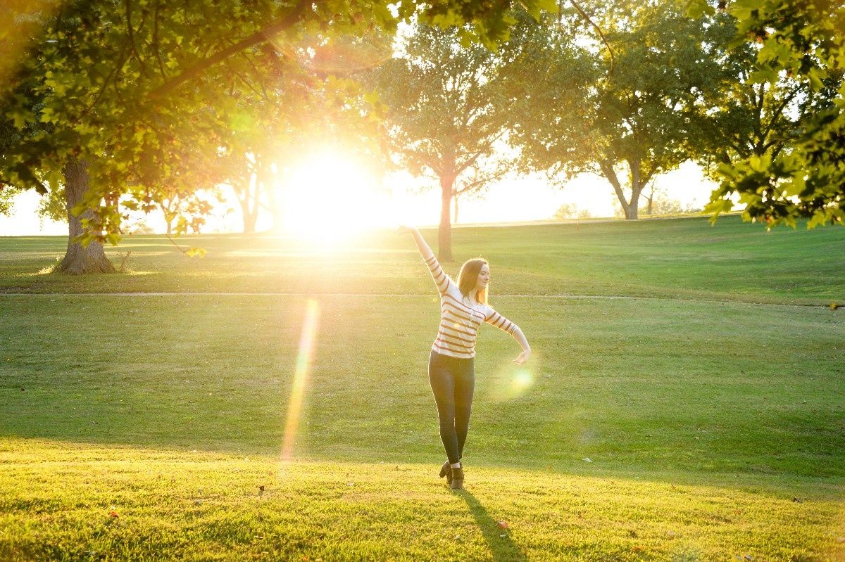 Person dancing in golden sunset light on grassy hill with trees.