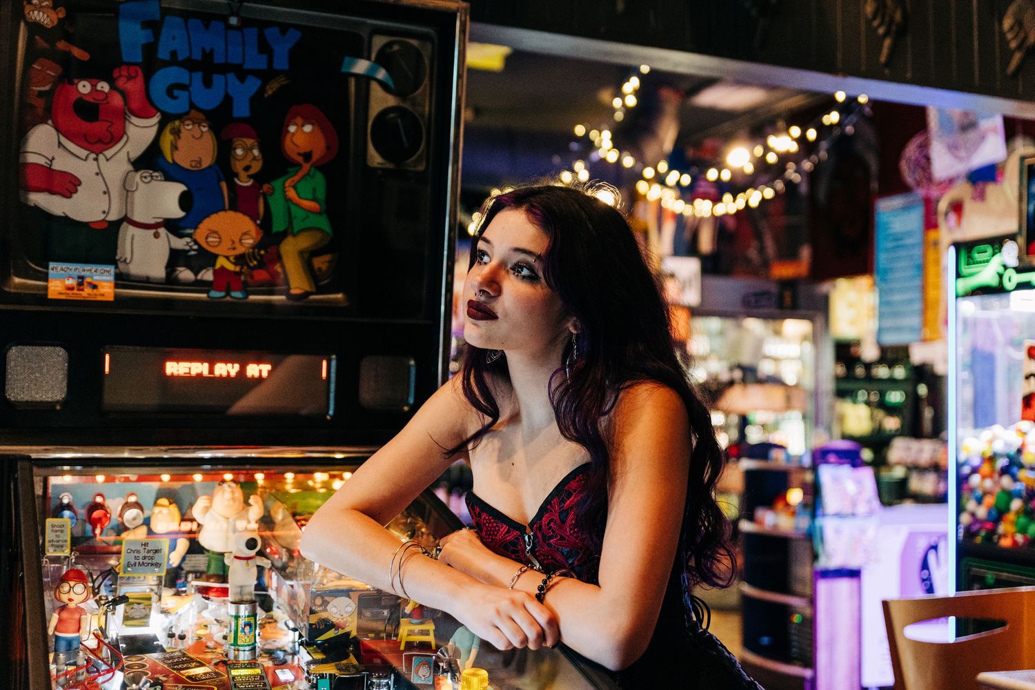A woman leans on a bar counter in a dimly lit establishment decorated with string lights and colorful memorabilia.
