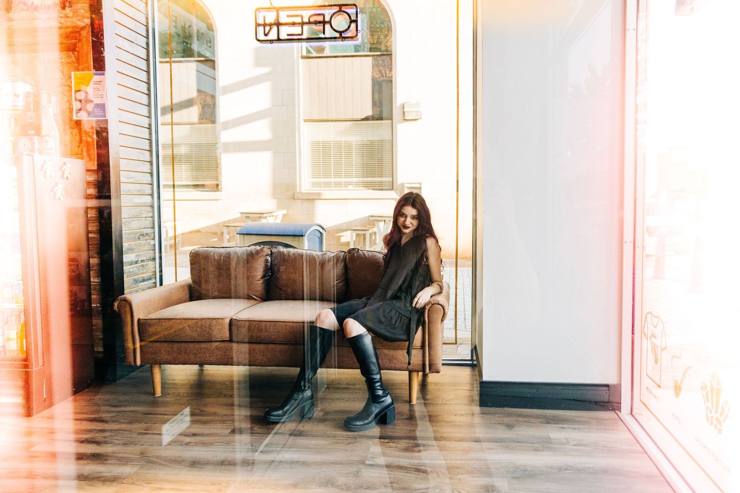 A stylish person sits alone in a modern cafe interior with wood floors and natural lighting through large windows.