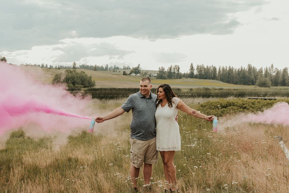 Celebrating gender reveal with pink powder smoke bombs in open field at outdoor photography venue in Spokane, Spokane family photographer