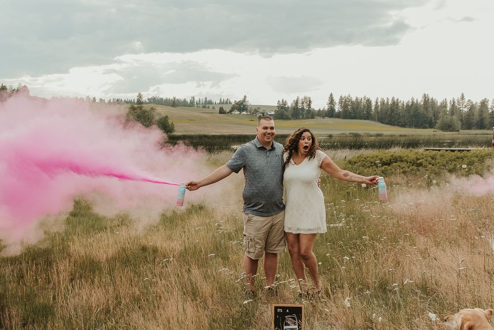 Celebrating gender reveal with pink powder smoke bombs in open field at outdoor photography venue in Spokane, Spokane family photographer
