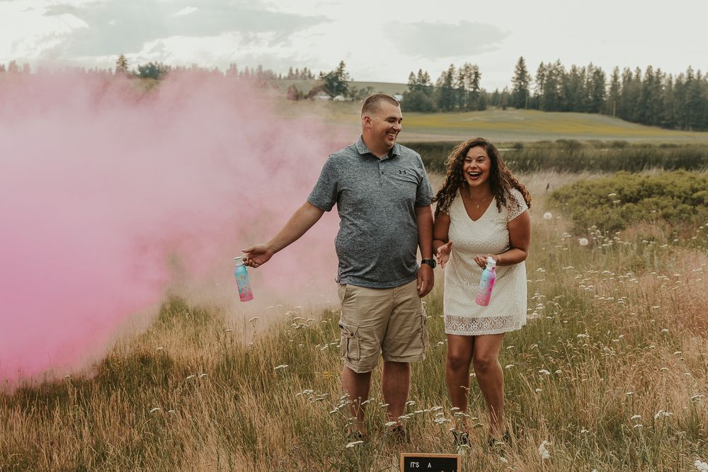 Celebrating gender reveal with pink powder smoke bombs in open field at outdoor photography venue in Spokane, Spokane family photographer