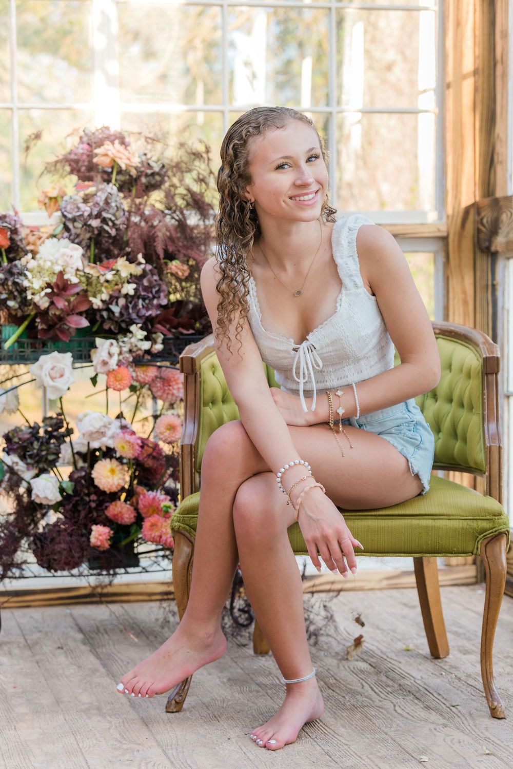 A series of boudoir photos showing someone posing on a green velvet chair with floral arrangements in a sunlit room.