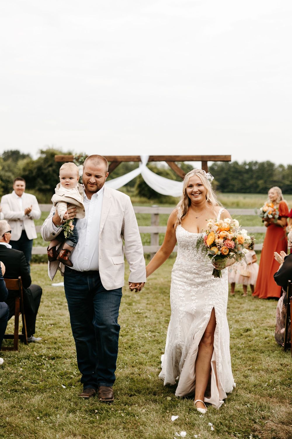 Wedding guests celebrate with couple during outdoor farm ceremony with colorful florals and rustic decor.