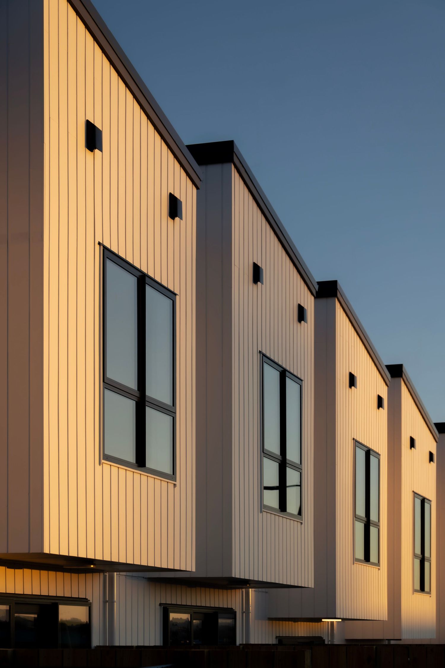 Row of contemporary cream-clad townhouses with black-framed windows, bathed in the soft golden light of sunset.