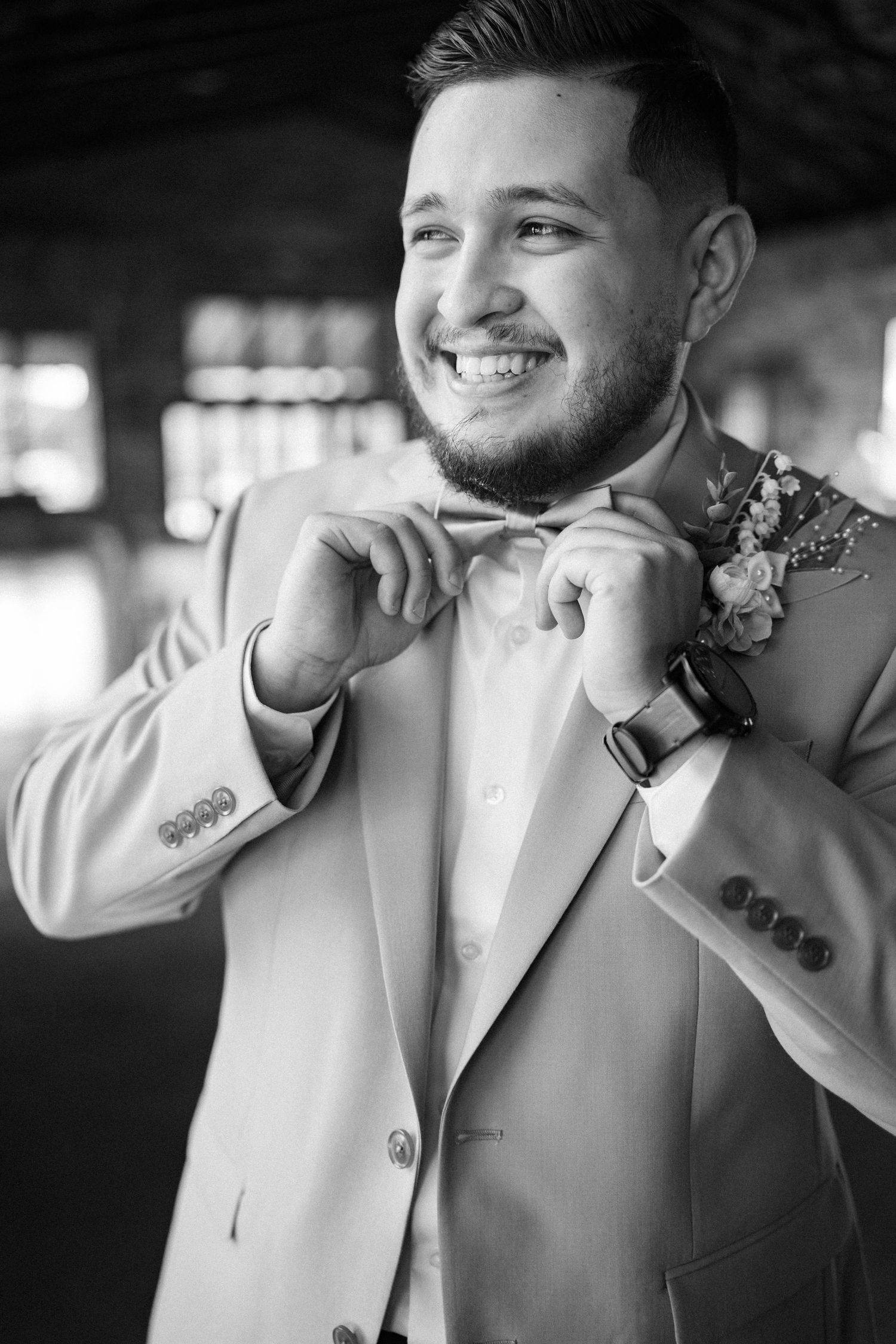 Black and white portrait of groom in light colored suit adjusting his collar.