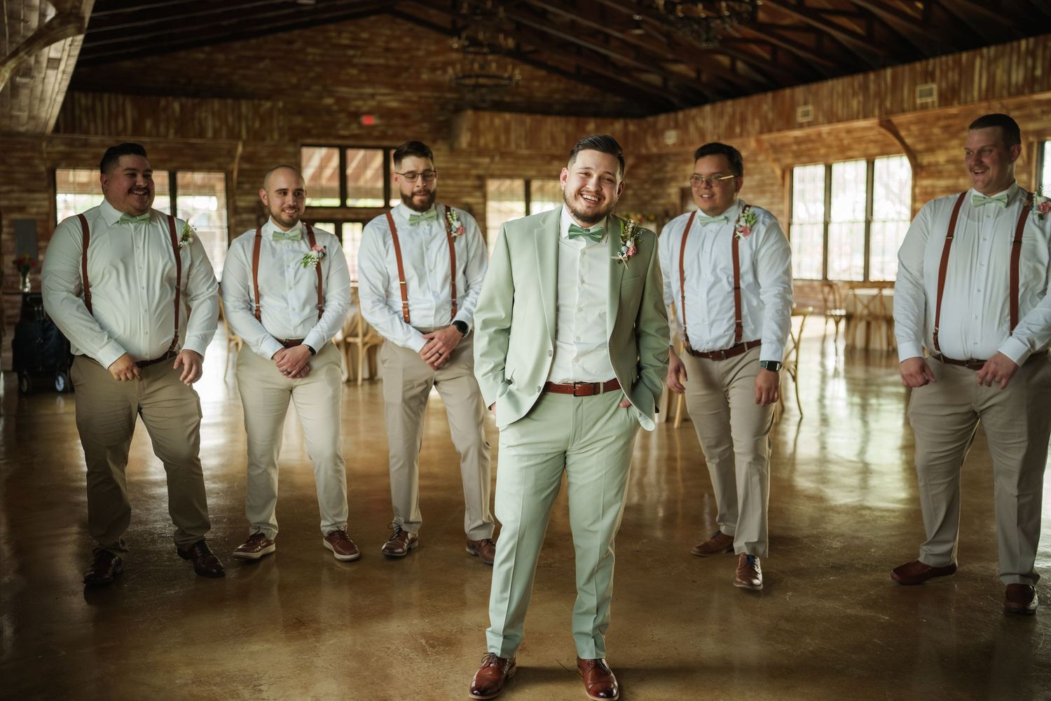 Groomsmen in light colored suits stand together in a rustic barn setting.