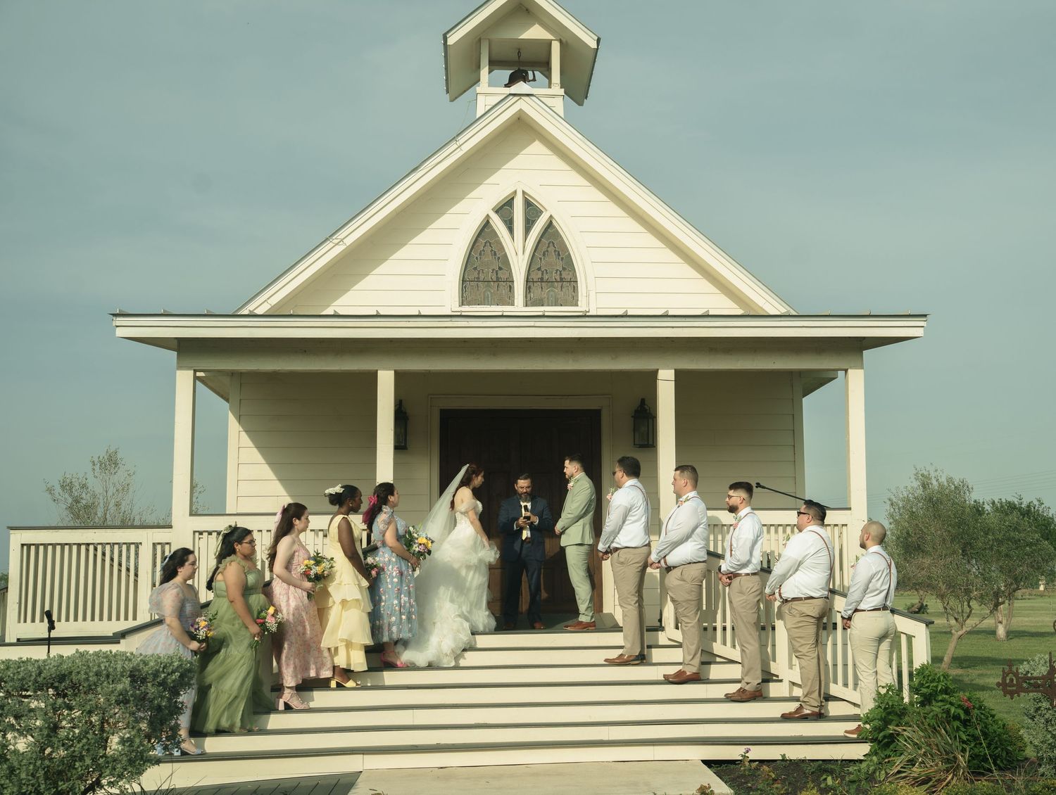 Wedding party poses on the white porch of a classic chapel-style building.