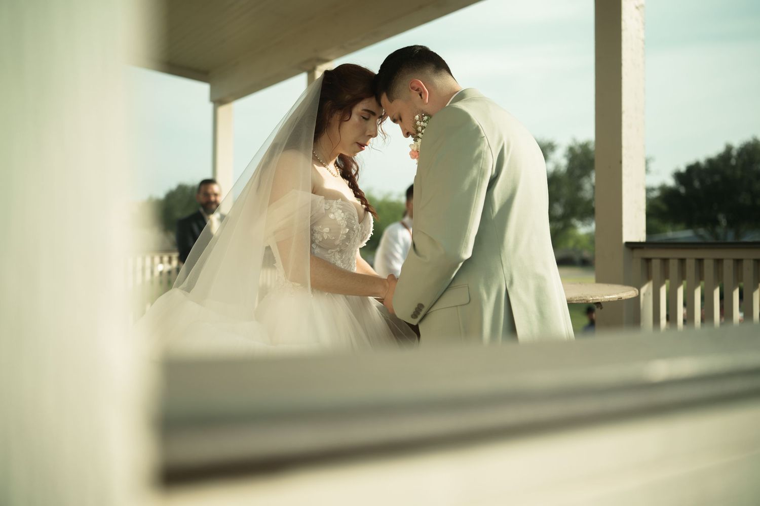 Intimate wedding portrait captured through architectural framing on a porch.