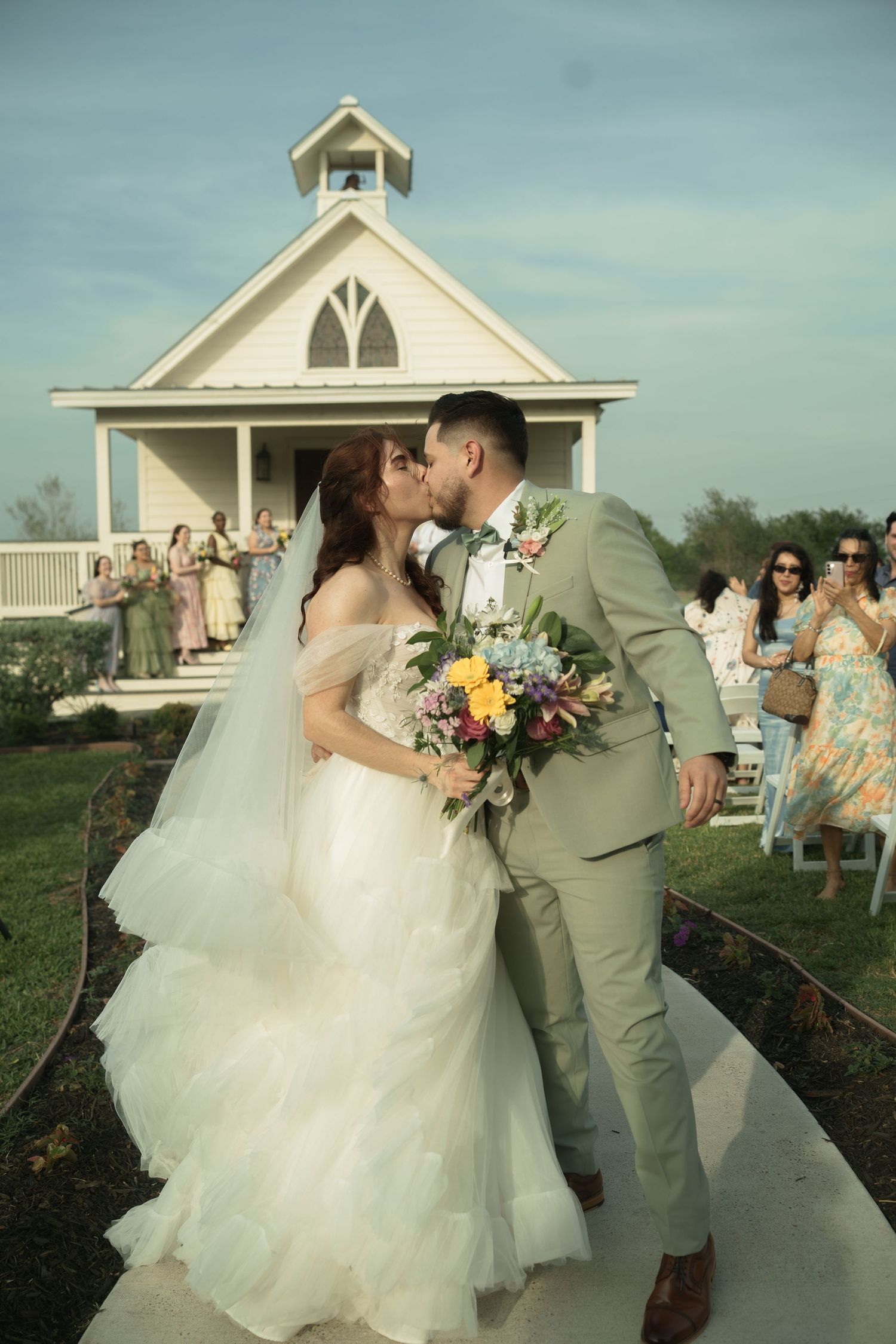 Newlyweds share romantic moments outside a white chapel building.
