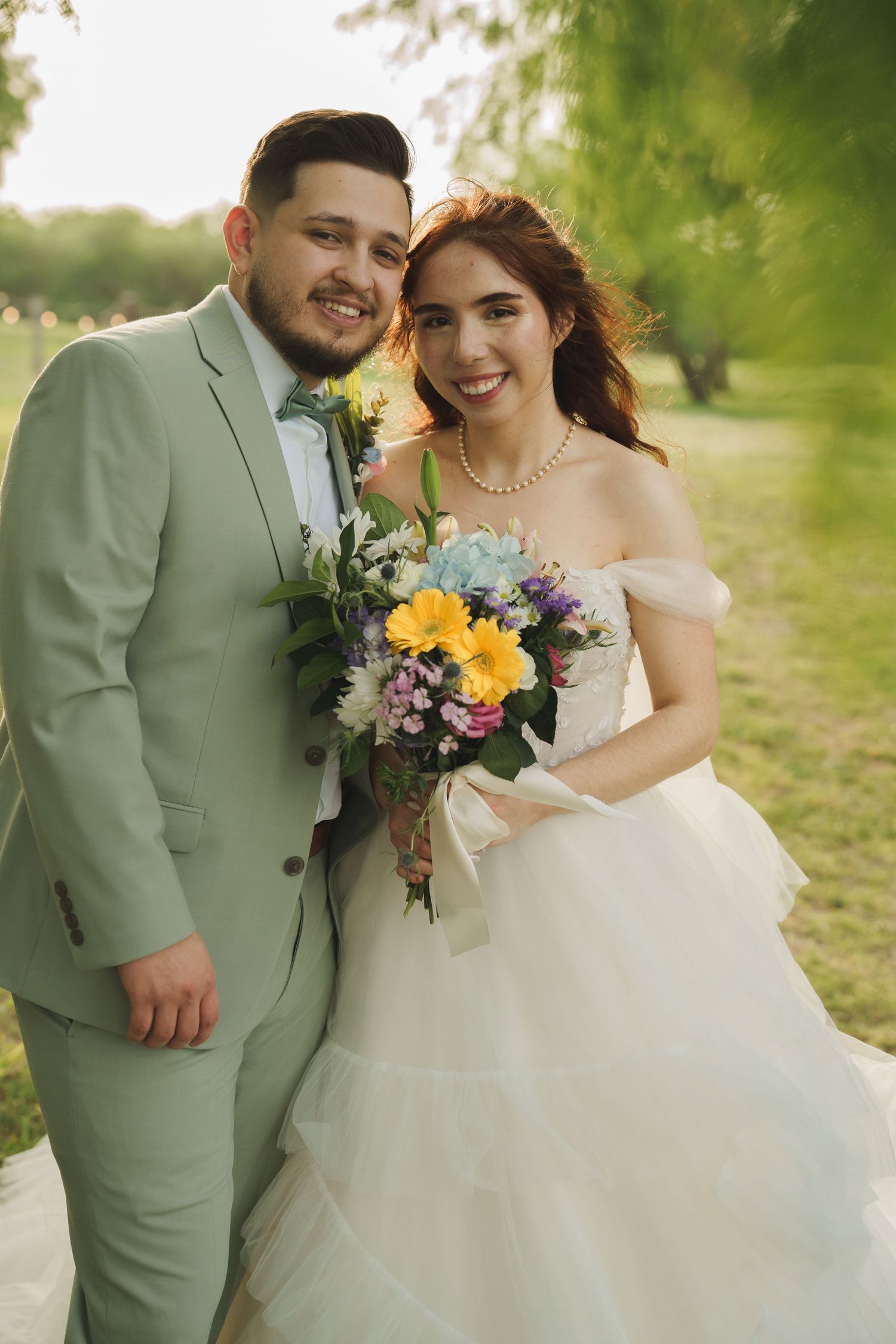 Spring wedding couple poses with colorful bouquet in outdoor setting.