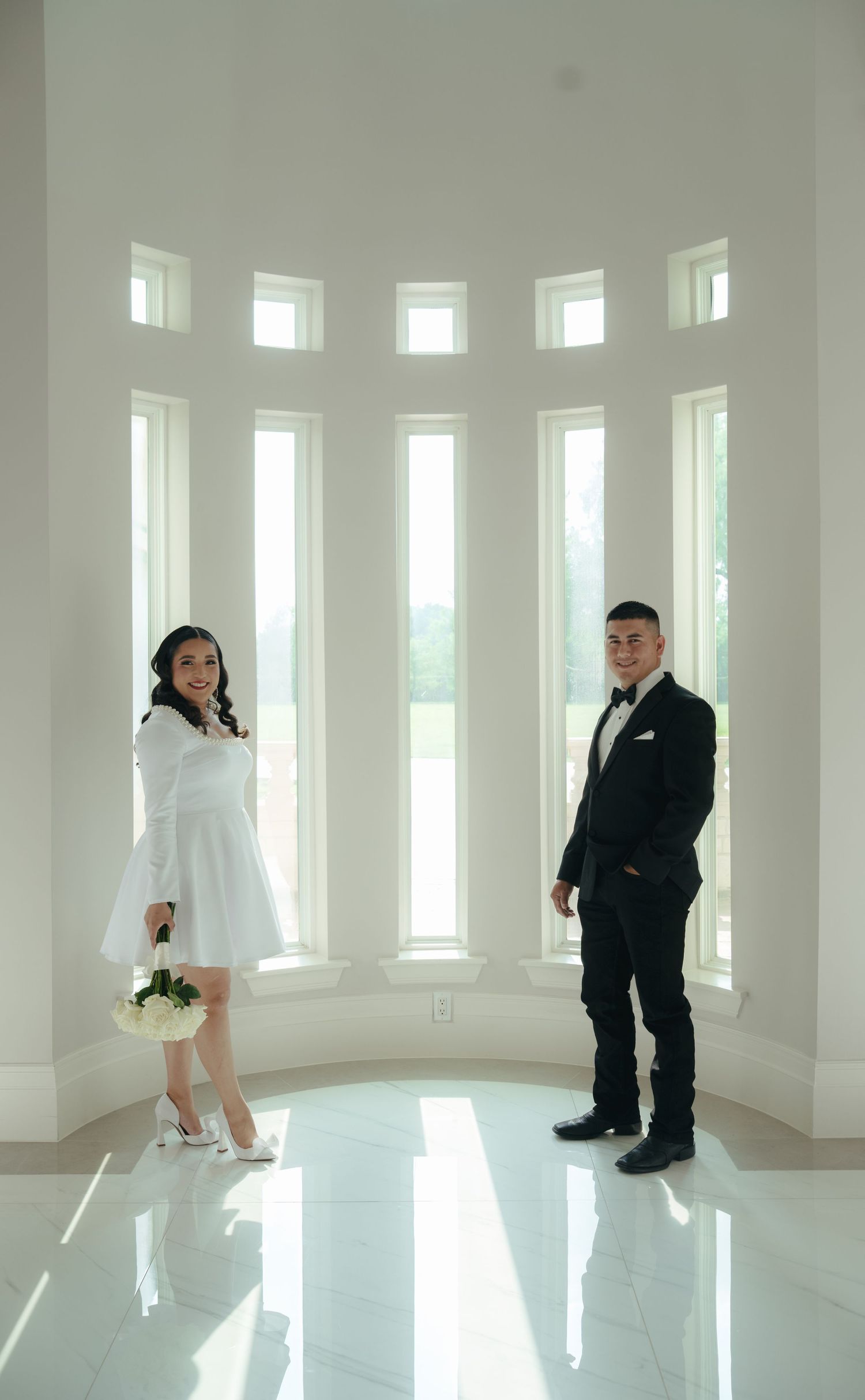 A wedding photoshoot in a bright white room with large windows and reflective floors.