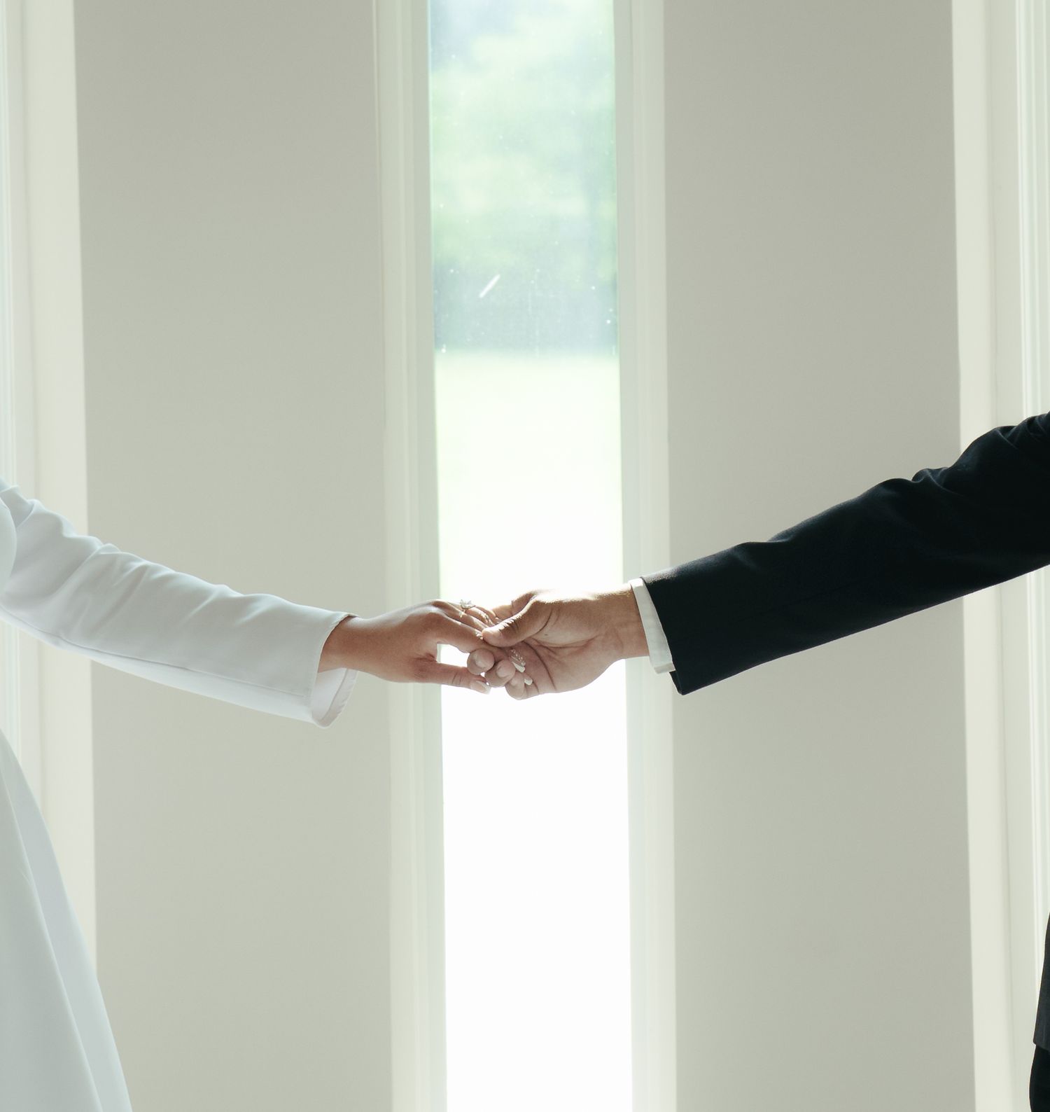 Close-up of hands reaching toward each other in a bright white room.