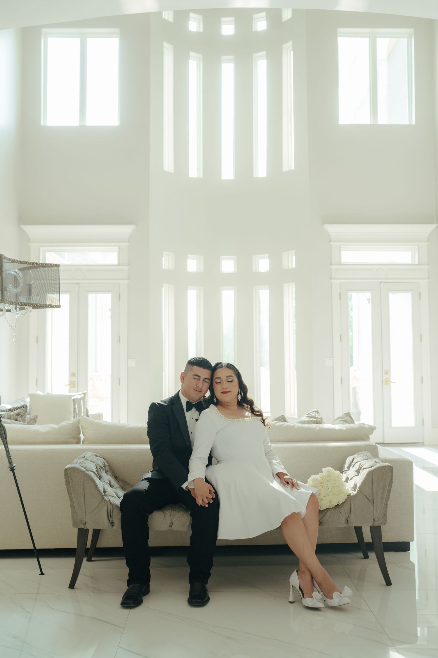 Newlyweds share intimate moments on a white sofa in a bright, airy room.