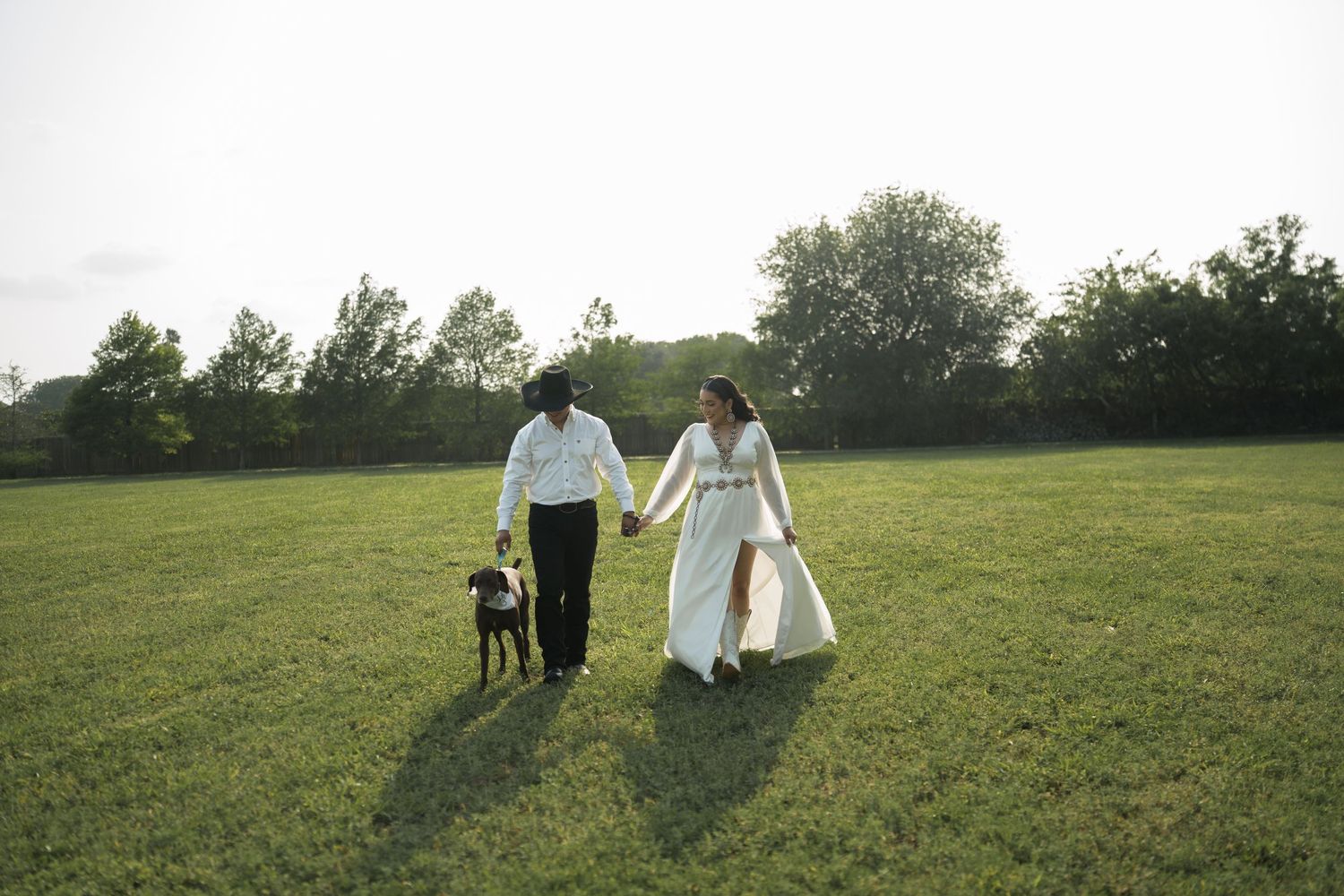 A couple strolls together across a scenic green field at sunset.