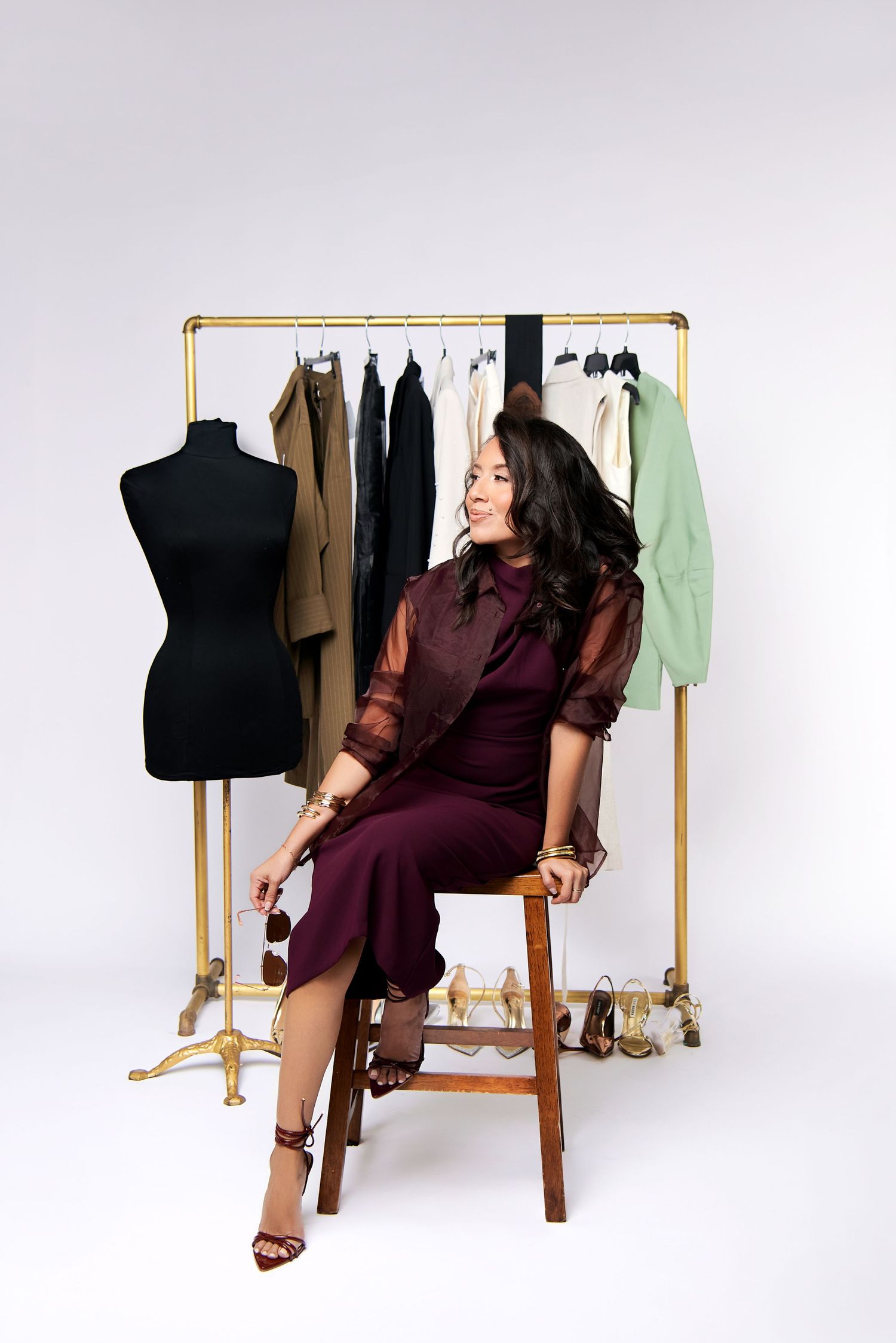 Woman in burgundy shirt sitting on wooden chair posing with black dress form mannequin in studio setting.