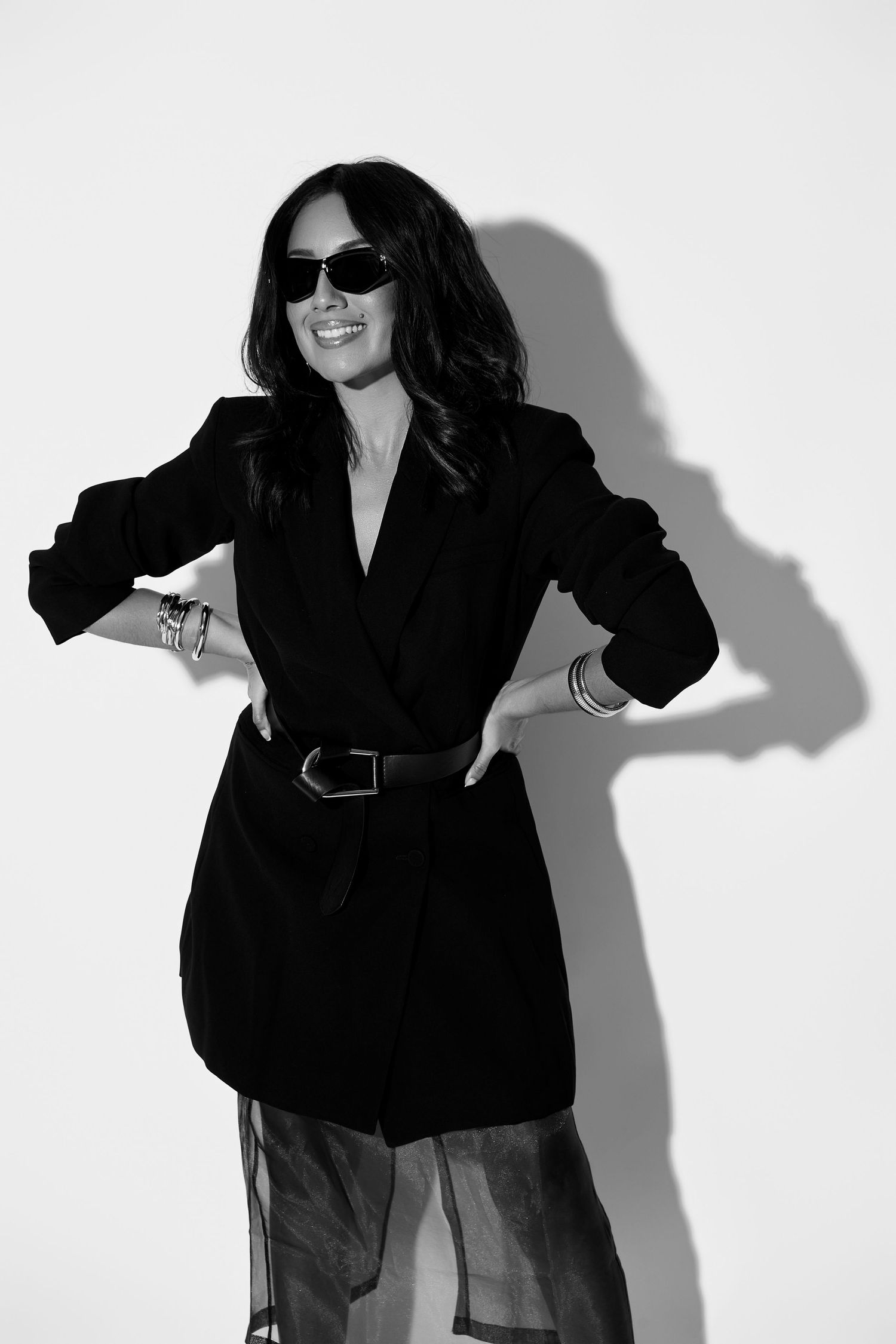 Fashion model poses in black blazer against white wall casting dramatic shadows in stylish editorial series.