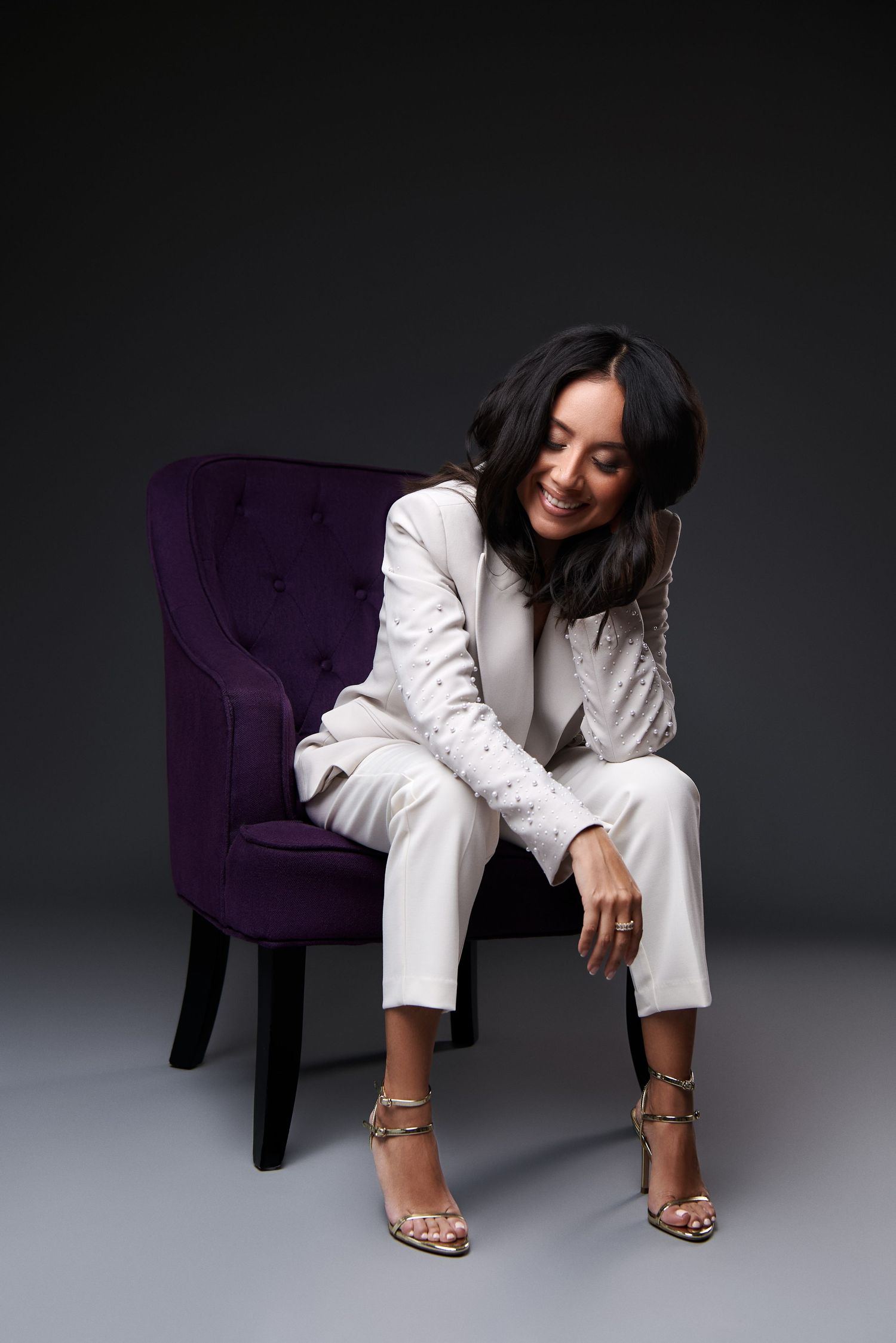 Four photos of a person in a white suit sitting on a purple velvet chair against a grey studio backdrop.